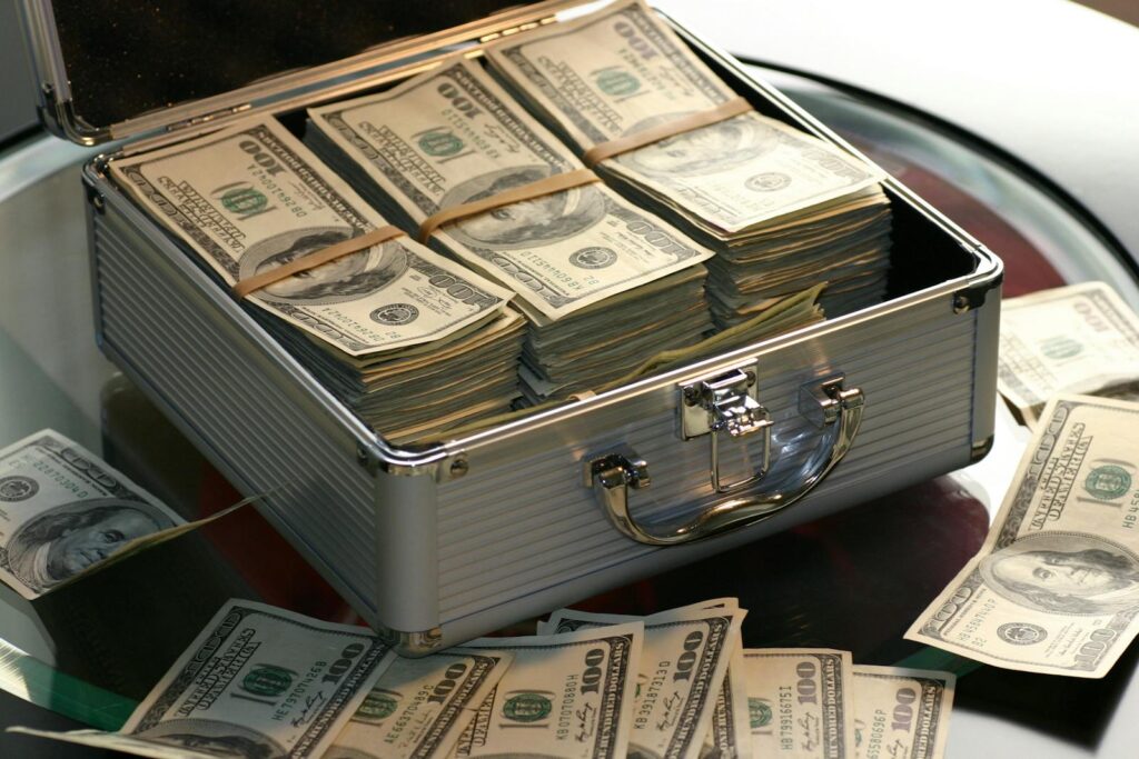 Photo by Pixabay Open briefcase filled with stacks of hundred dollar bills on a glass table, representing wealth.