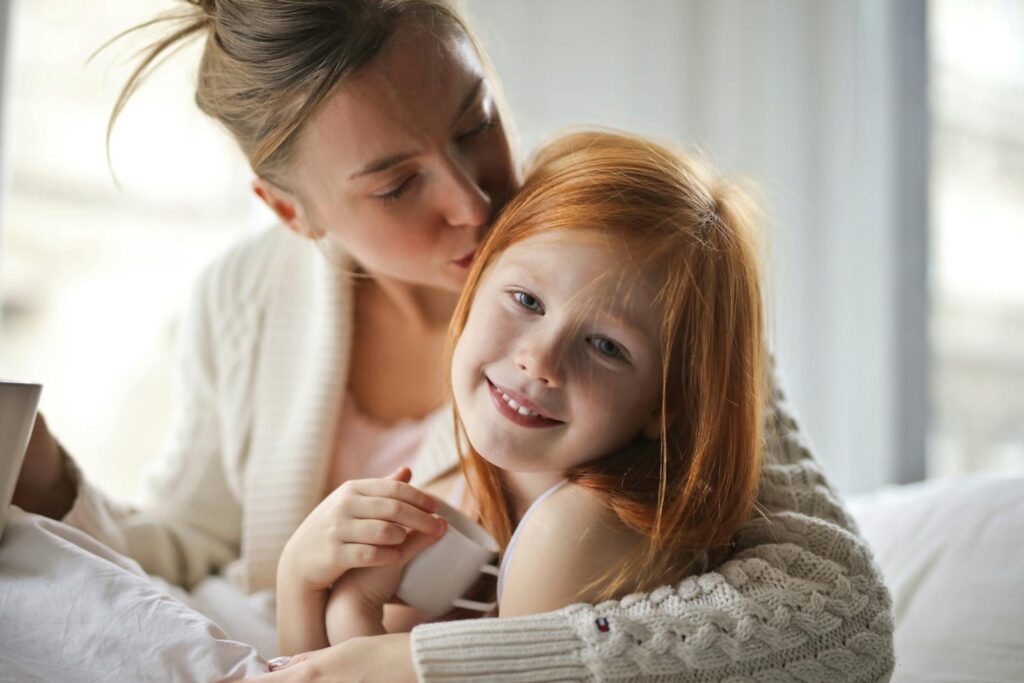 Photo by Andrea Piacquadio A mother tenderly hugging her smiling daughter indoors, showcasing love and warmth.