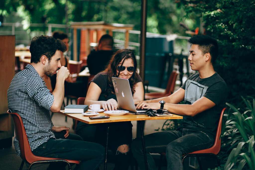 Photo by Helena Lopes A group of young adults working on a laptop at an outdoor coffee shop, enjoying teamwork and collaboration.